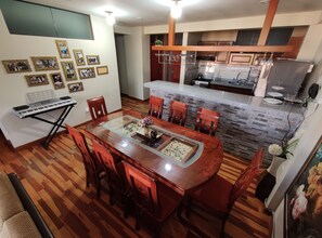 A dining area with a wooden table and chairs, a piano, and framed photos on the wall. - El Balcón del Sol (Cusco)