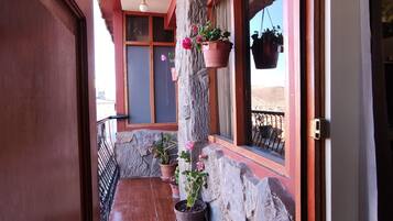 A corridor with a tiled floor, stone wall, and wooden beams. There are potted plants along the wall and hanging baskets.