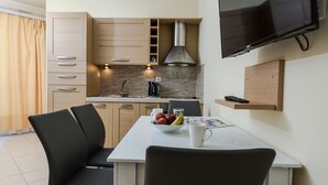 A compact kitchen with a dining area, featuring a TV mounted on the wall, a coffee maker, and a bowl of fruit on the table. - Waterfront apartment 4 (Κίσσαμος)