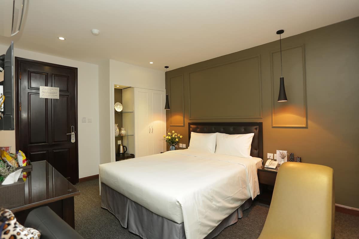 A hotel room with a large bed, a desk, a chair, and a wardrobe.
