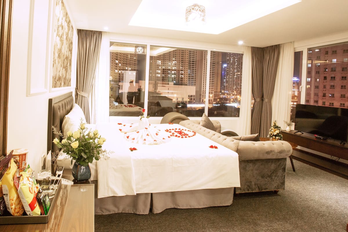 A hotel room with a large bed, a sofa, a TV, and a city view.
