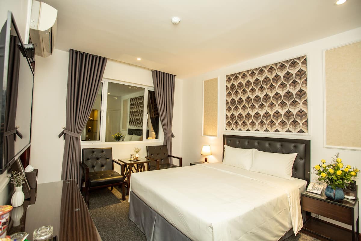 A hotel room with a large bed, a desk with a chair, a small table, a lamp, and a telephone.