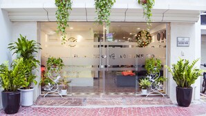 Entrada de hotel con plantas en macetas, puerta de cristal y un letrero que indica un restaurante.