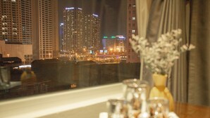 Vista desde una ventana que da a un paisaje urbano nocturno, con edificios altos con ventanas y letreros iluminados.