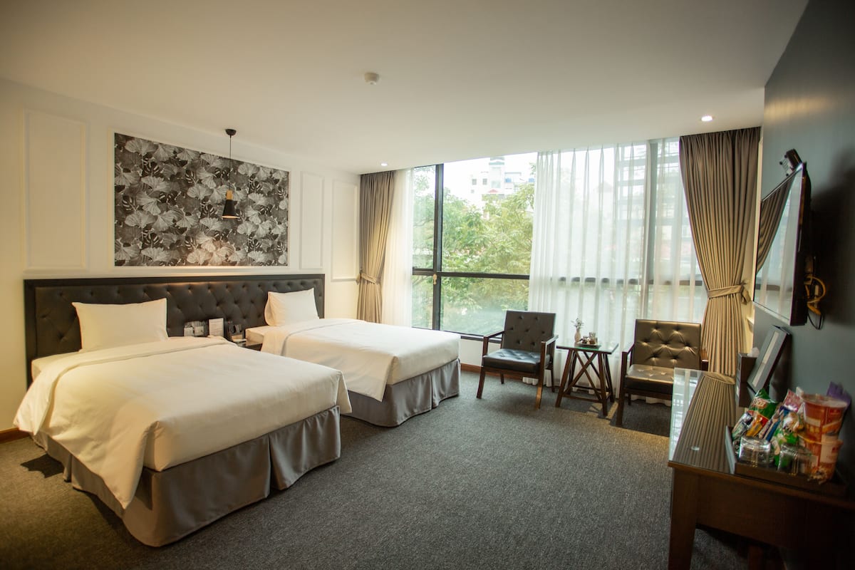 A hotel room with two beds, a desk, a chair, a TV, and a large window with curtains.