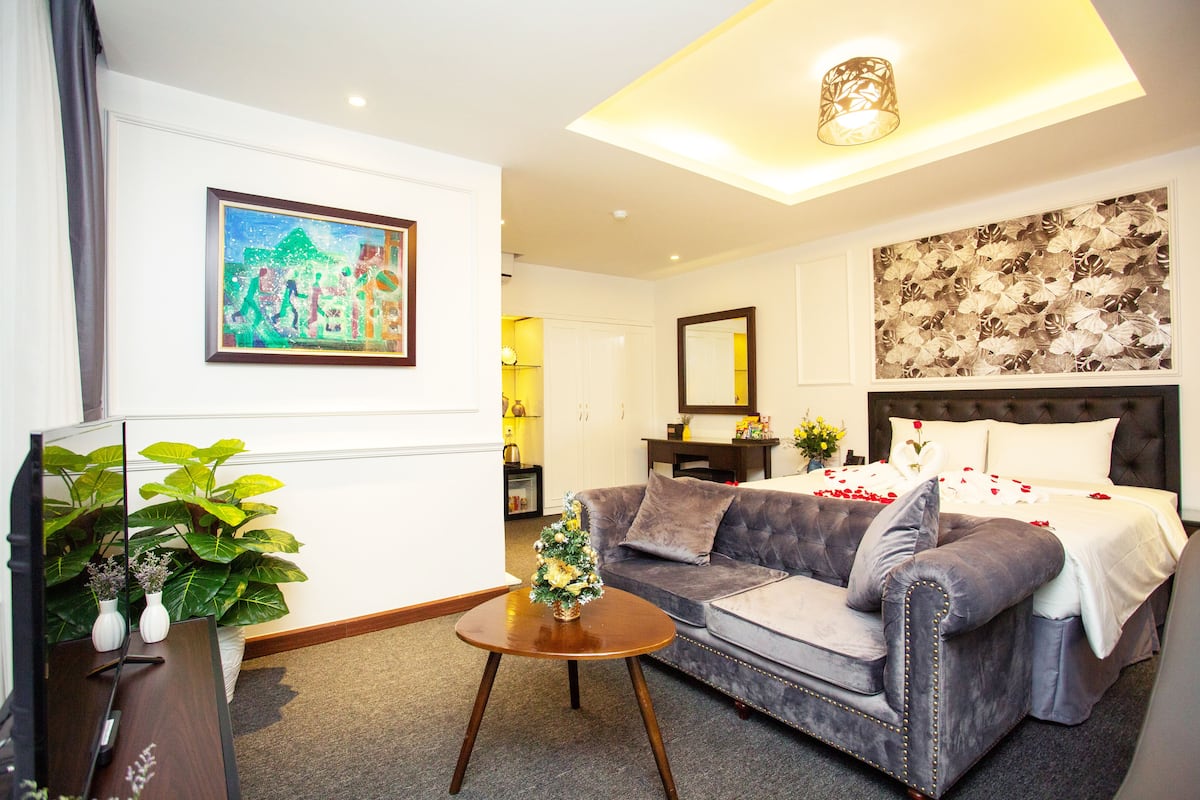 A hotel room with a large bed, a sofa, a small table, a mirror, and a painting on the wall.