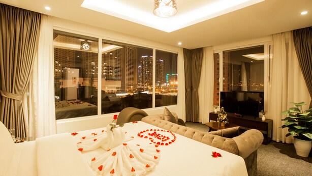 Habitación de hotel con una cama grande, televisión, sofá y vista de la ciudad de noche.