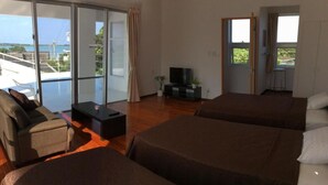 Habitación de hotel con dos camas, un sofá, un televisor y un balcón con vistas al mar.