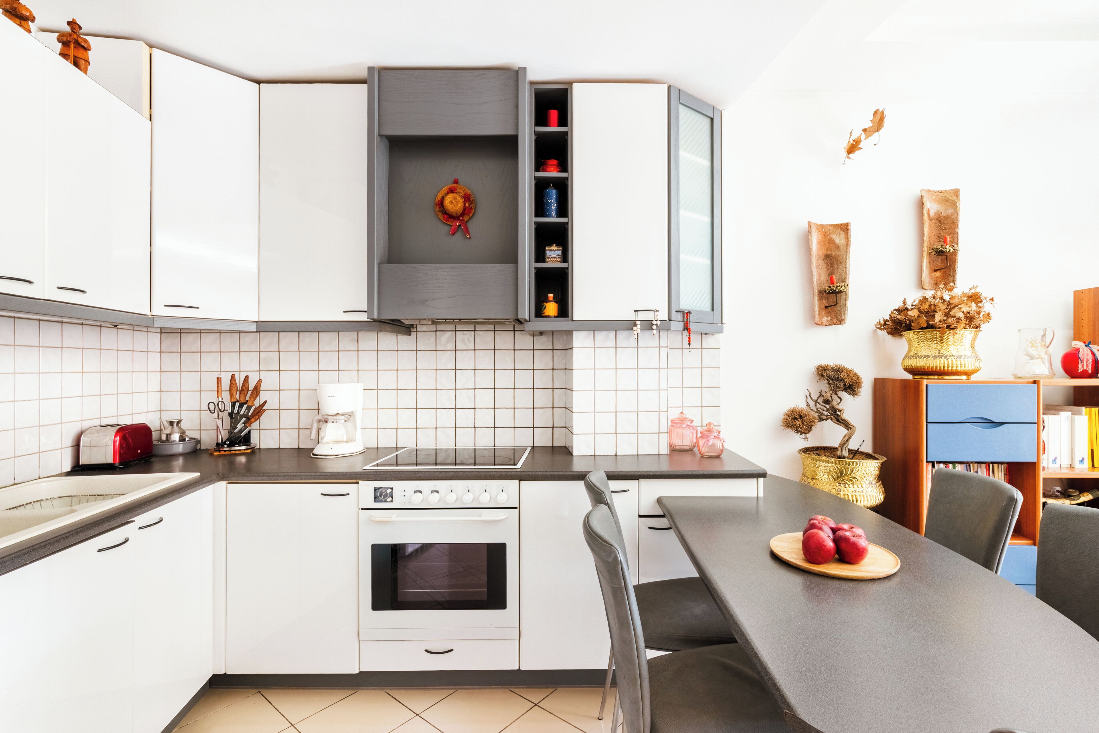 Een moderne keuken met witte kastjes, een ingebouwde oven en een eethoek met een tafel en stoelen.