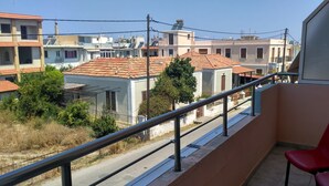 A balcony with a metal railing overlooking a residential area with houses and a road. - Apartment "Grace" with 2 spaces, at the foothills of Filerimos, Ialysos - Rhodes (Ιαλυσός)