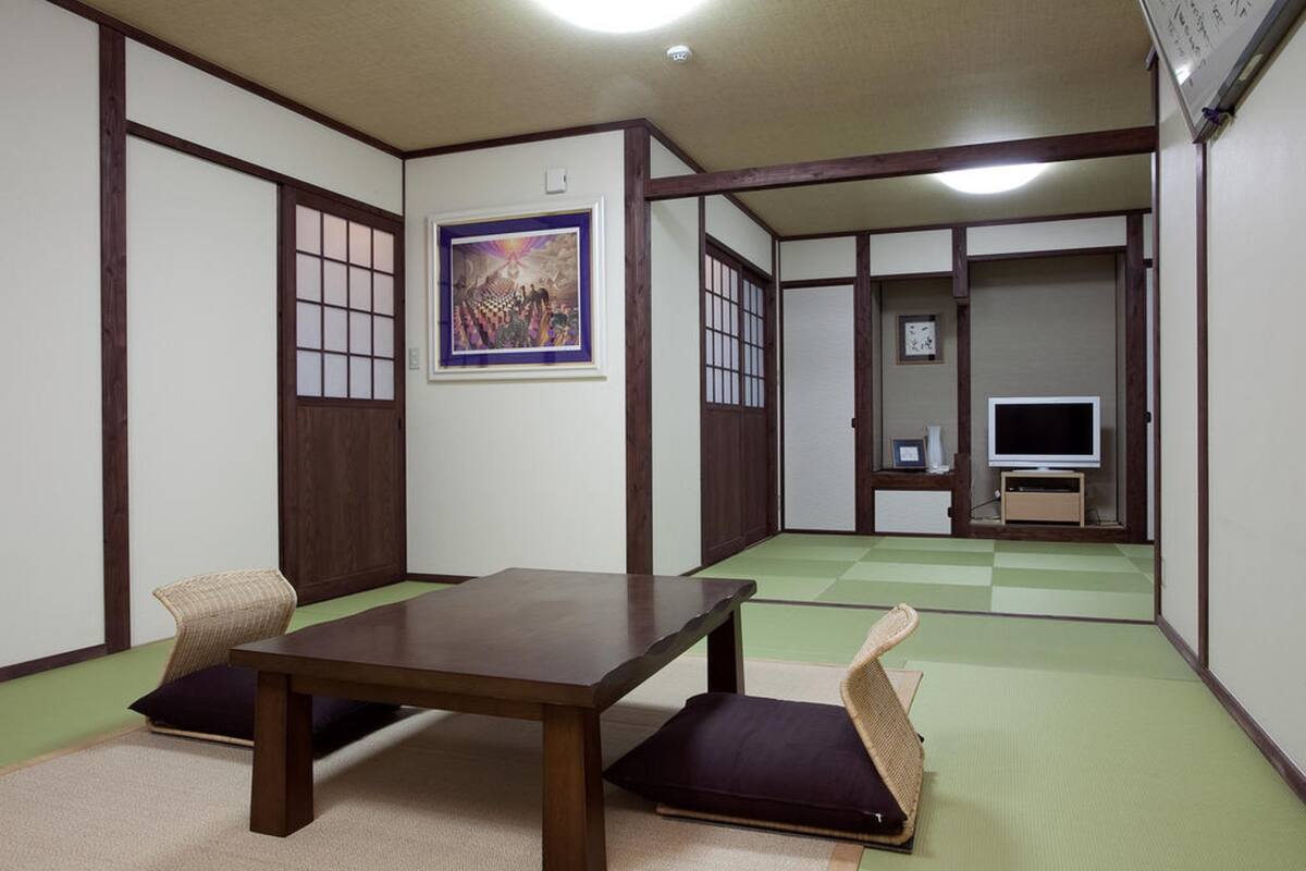 A traditional Japanese room with tatami flooring, a low table, cushions, a television, and a framed artwork on the wall.