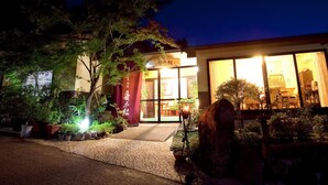 A traditional Japanese building with a well-lit entrance and a garden area with potted plants. - Yufuin Sanso Waremokou (Yufu)