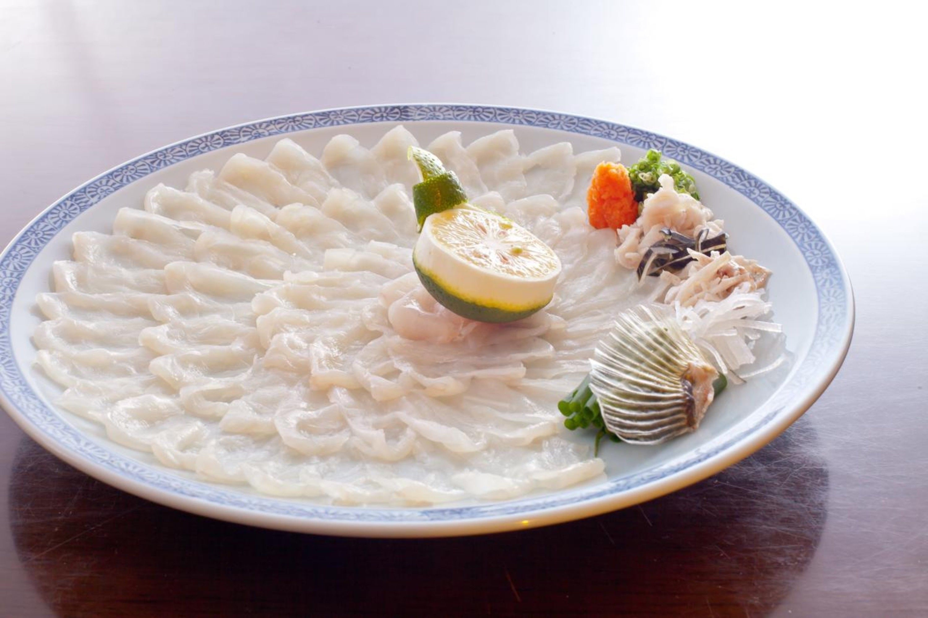Un plato de comida con varios elementos, incluyendo pescado, verduras y una rodaja de cítricos.