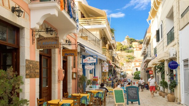 Una calle con mesas al aire libre, un restaurante llamado “O Mita” y diversas tiendas.