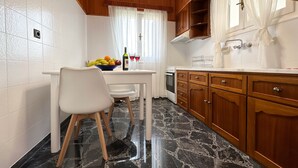 Una cocina compacta con mesa de comedor, armarios de madera, piso de mármol y ventana con cortinas traslúcidas.