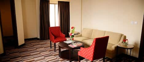 Une chambre d’hôtel avec une moquette à motifs, un canapé beige, deux fauteuils rouges, une table basse et une petite table d’appoint sur laquelle est posé un vase de fleurs.