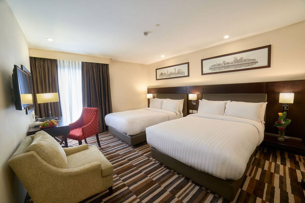 Ett hotellrum med två sängar, en soffa, en TV och ett skrivbord med en lampa.