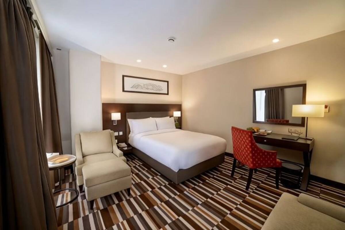 A hotel room with a bed, a desk, a chair, a small table, and a mirror.