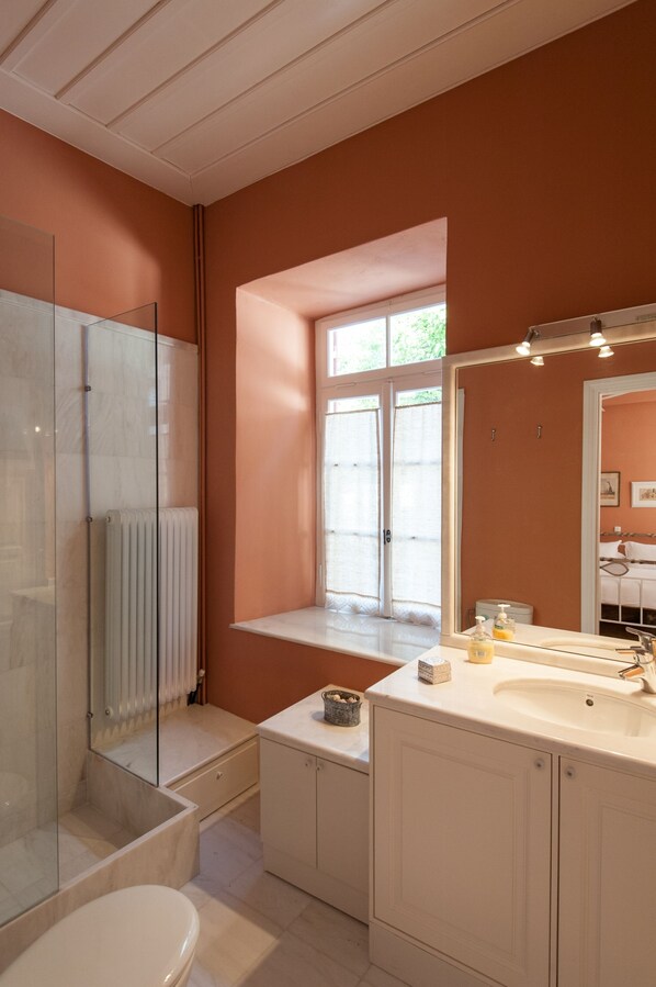 A bathroom with a glass shower enclosure, a window with a view, a sink with a mirror, and a toilet. - Fully Renovated With All Modern Comforts. (Ναύπλιο)