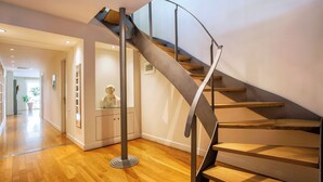 Un interno moderno con una scala a chiocciola, pavimento in legno e una vetrina che ospita una scultura.