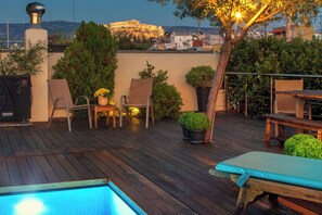 Une terrasse sur le toit avec une piscine, des chaises longues, une table et des plantes en pot.