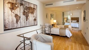 Camera d'albergo con un'ampia opera d'arte raffigurante una mappa del mondo, una scrivania, due letti e una porta vetrata che dà su un'altra stanza.