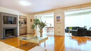 Un soggiorno moderno con camino, televisore a schermo piatto, tavolino in vetro e divano. Si intravede un'area pranzo con tavolo e sedie attraverso un'apertura.