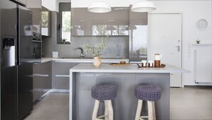 Une cuisine moderne dotée d’un îlot central, d’appareils électroménagers en acier inoxydable, de luminaires suspendus et offrant une vue sur l’extérieur.