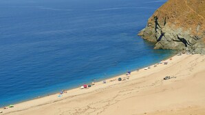 Une plage à l’eau d’un bleu limpide, avec un rivage sablonneux et des falaises rocheuses.