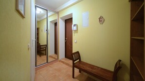 A hallway with a wooden bench, a door, and a mirror reflecting a room with a chair.