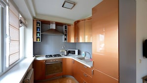 A compact kitchen with a stove, microwave, and oven, featuring wooden cabinets and a window with blinds.