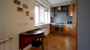 A compact kitchen with a dining area, a window with blinds, and a radiator.