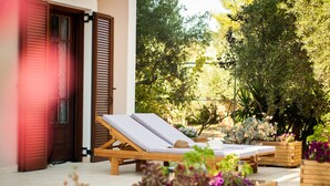 Une terrasse en bois avec deux chaises longues, une porte en bois et un jardin agrémenté de diverses plantes.