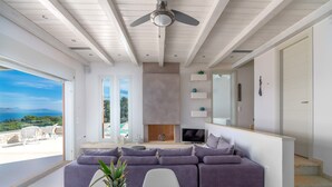 A modern living room with a sofa, a TV, and a view of the sea. - Villa Emmelia & Guesthouse Amazing View With Pool (Πόρτο Χέλι)