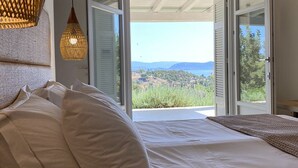 A bedroom with a large bed, a view of the outdoors, and a hanging light fixture. - Villa Emmelia & Guesthouse Amazing View With Pool (Πόρτο Χέλι)