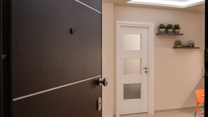 Un interno moderno con una porta in legno scuro, una porta bianca con pannelli di vetro, un pavimento piastrellato e una piccola sedia arancione.