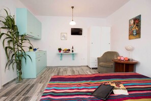 Un dormitorio con cama, escritorio, silla, televisor y una planta.