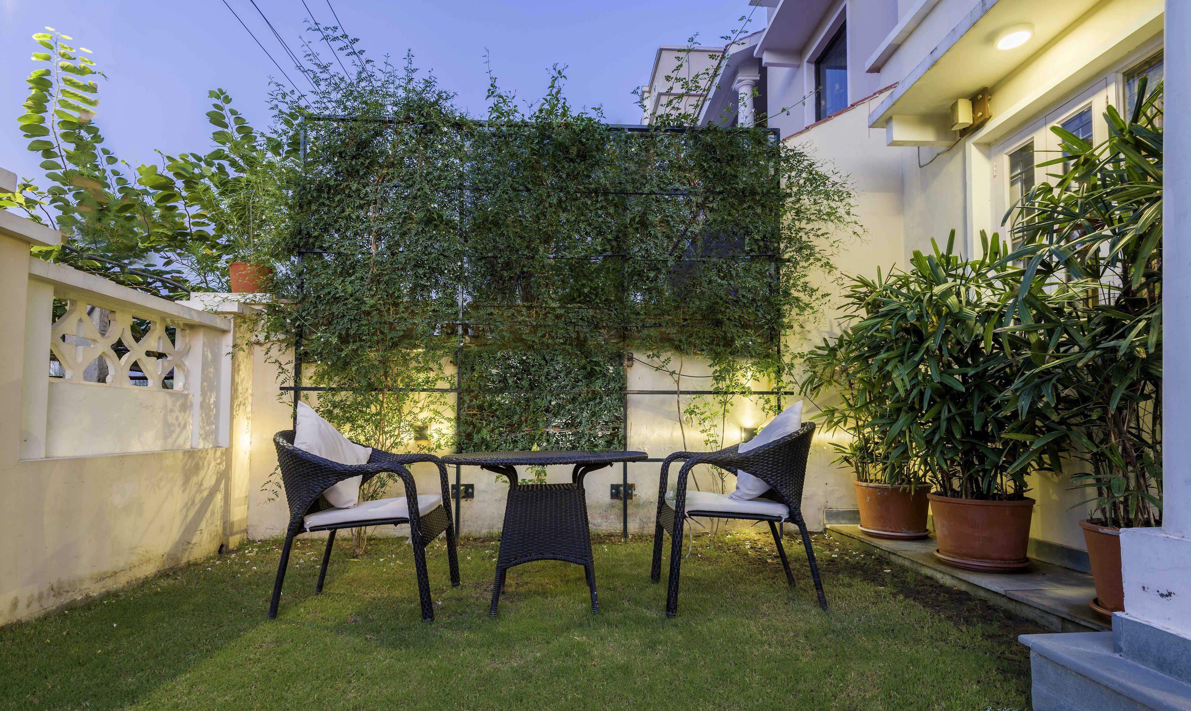 A small outdoor seating area with wicker chairs and a table, surrounded by potted plants and a wall covered in climbing plants.