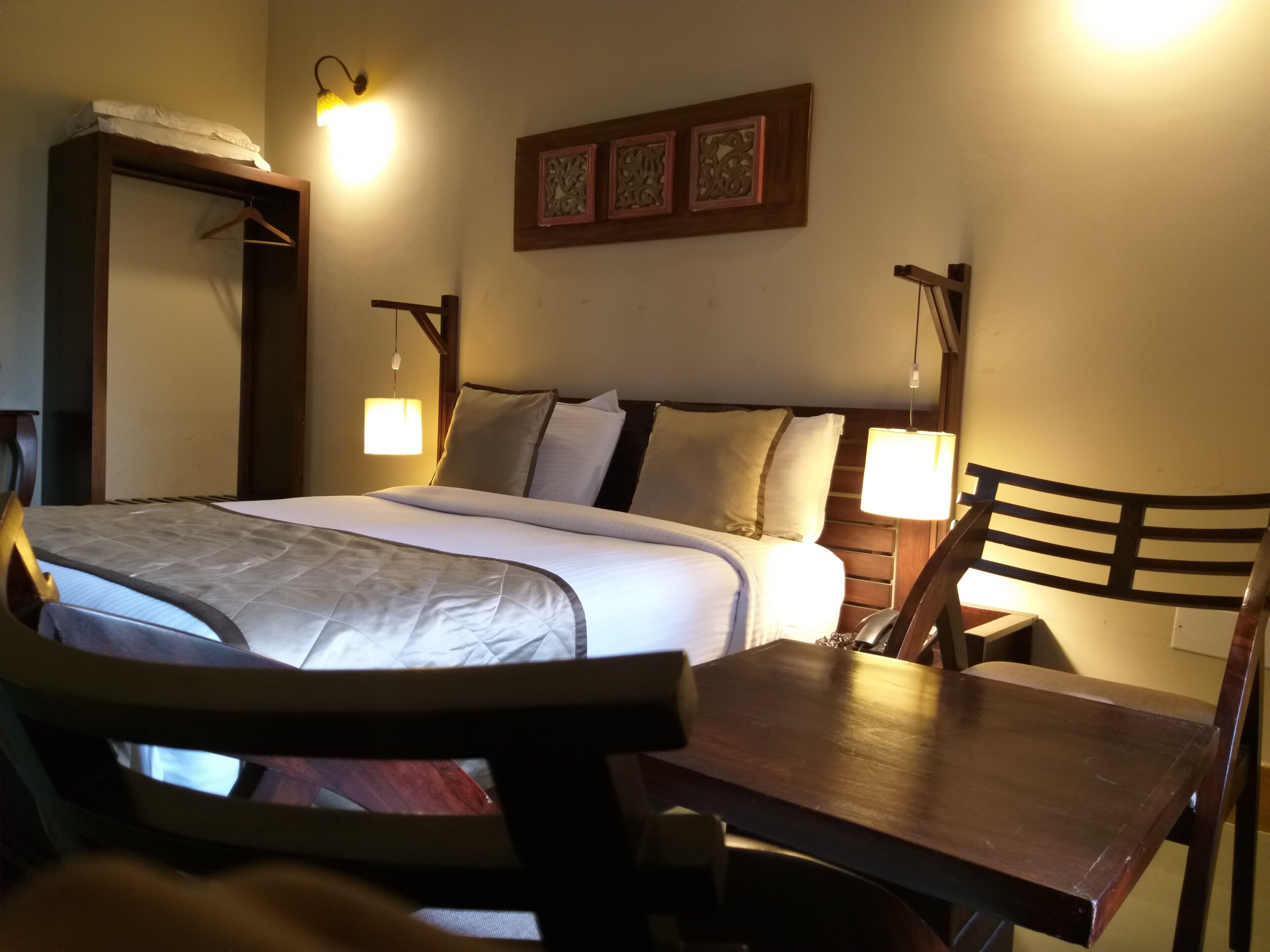 A hotel room with a bed, bedside lamps, a wooden chair, and a table.