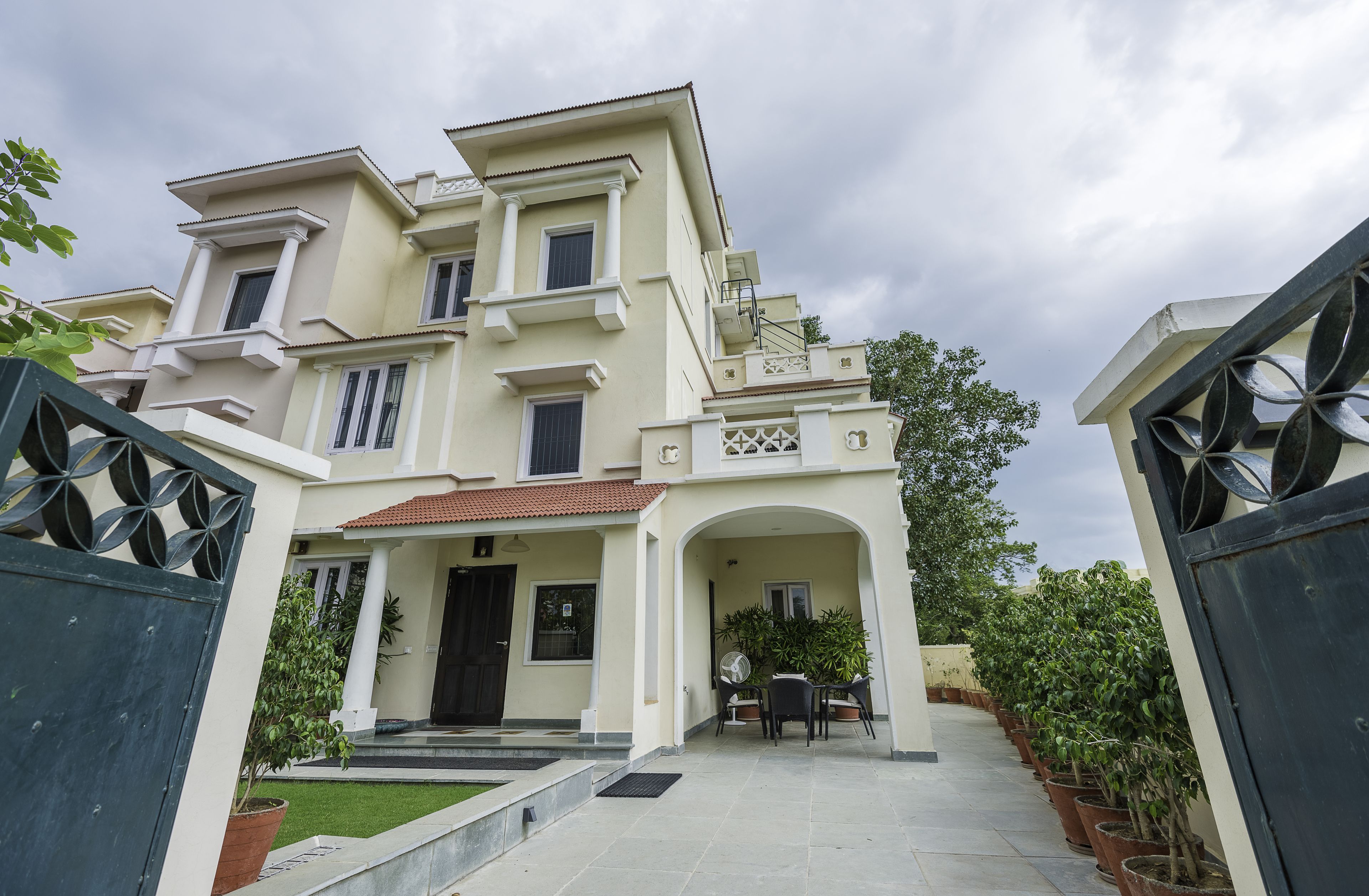 A multi-story house with a tiled roof, a front porch, and a garden with potted plants.