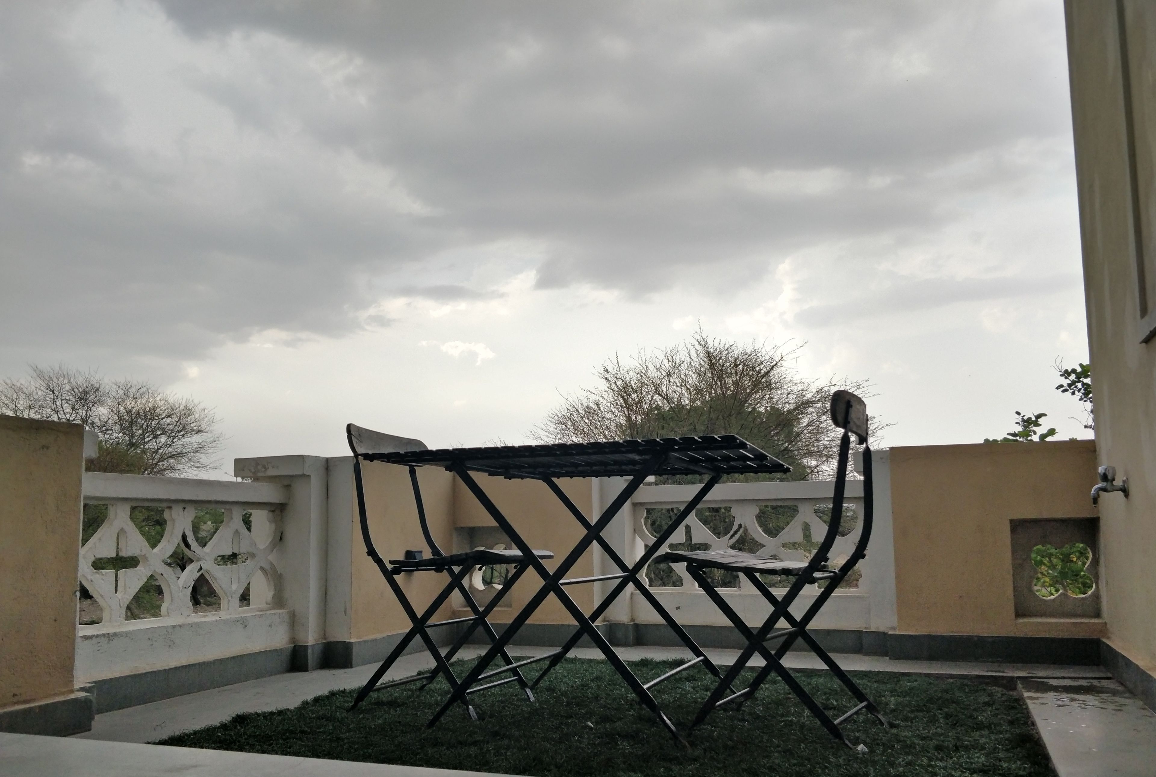 A metal folding table in an outdoor area with a white decorative fence and a beige wall in the background.