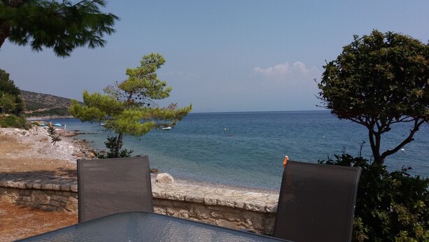 A seaside view with a stone wall, two chairs, and a table overlooking the sea.