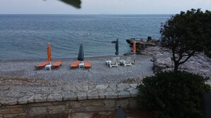 A pebble beach with lounge chairs and umbrellas facing the sea.