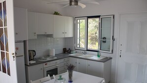 A compact kitchen with white cabinets, a stove, a sink, and a window with a view of greenery outside.