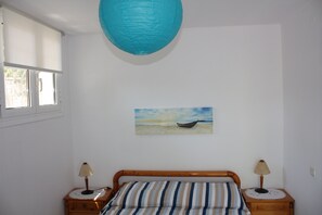 Een slaapkamer met een bed, twee nachtkastjes, een raam en een schilderij van een boot op het strand.
