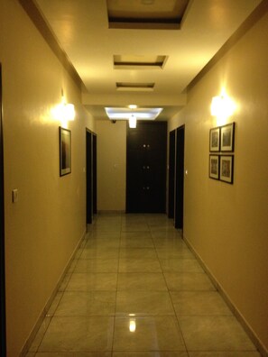 A hotel hallway with a tiled floor, light fixtures on the walls, and a door at the end. - Hotel Plaza Inn Ajmer (Ajmer)