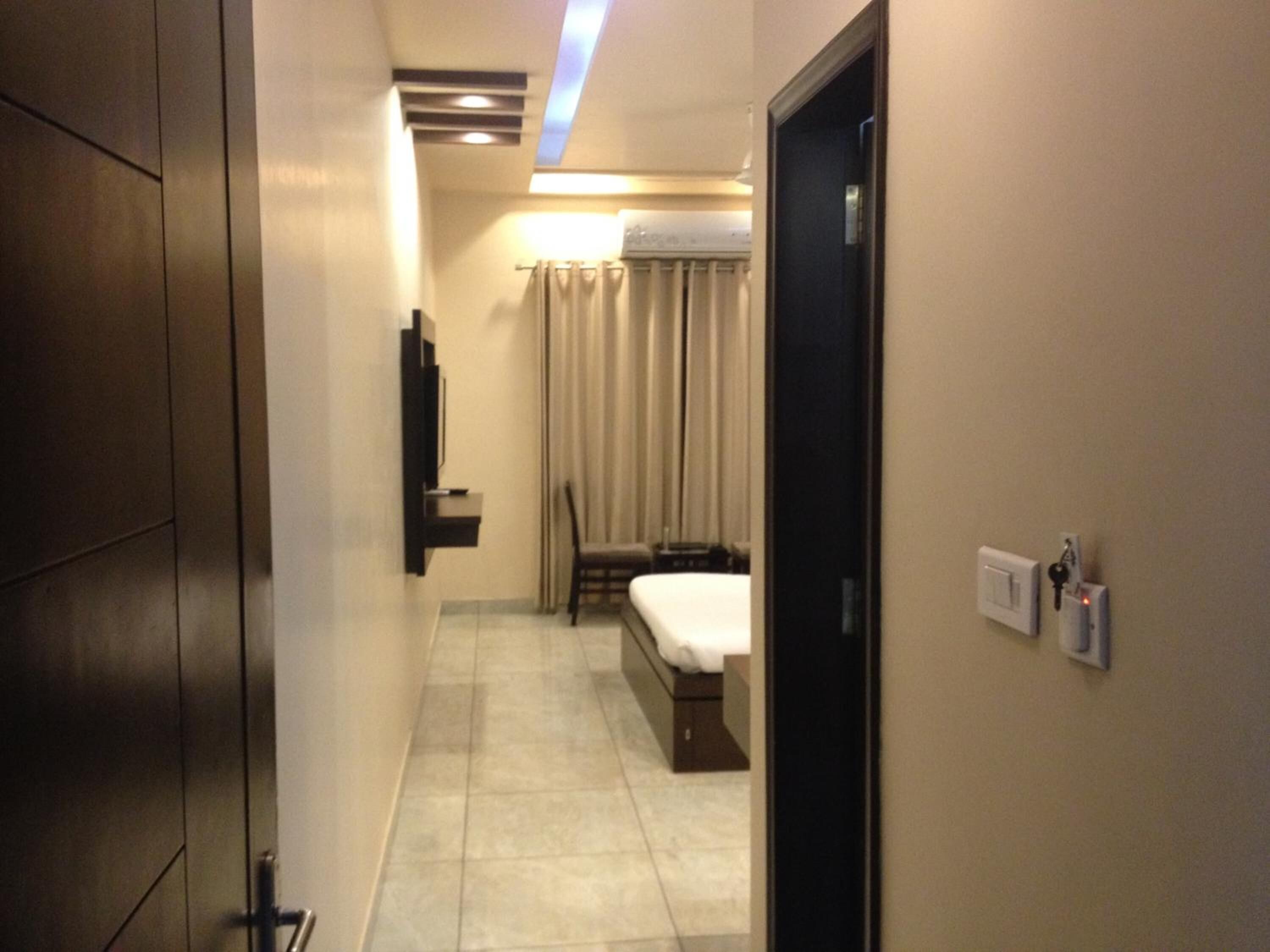 A narrow hallway leading to a bedroom with a bed, a chair, and a television mounted on the wall.