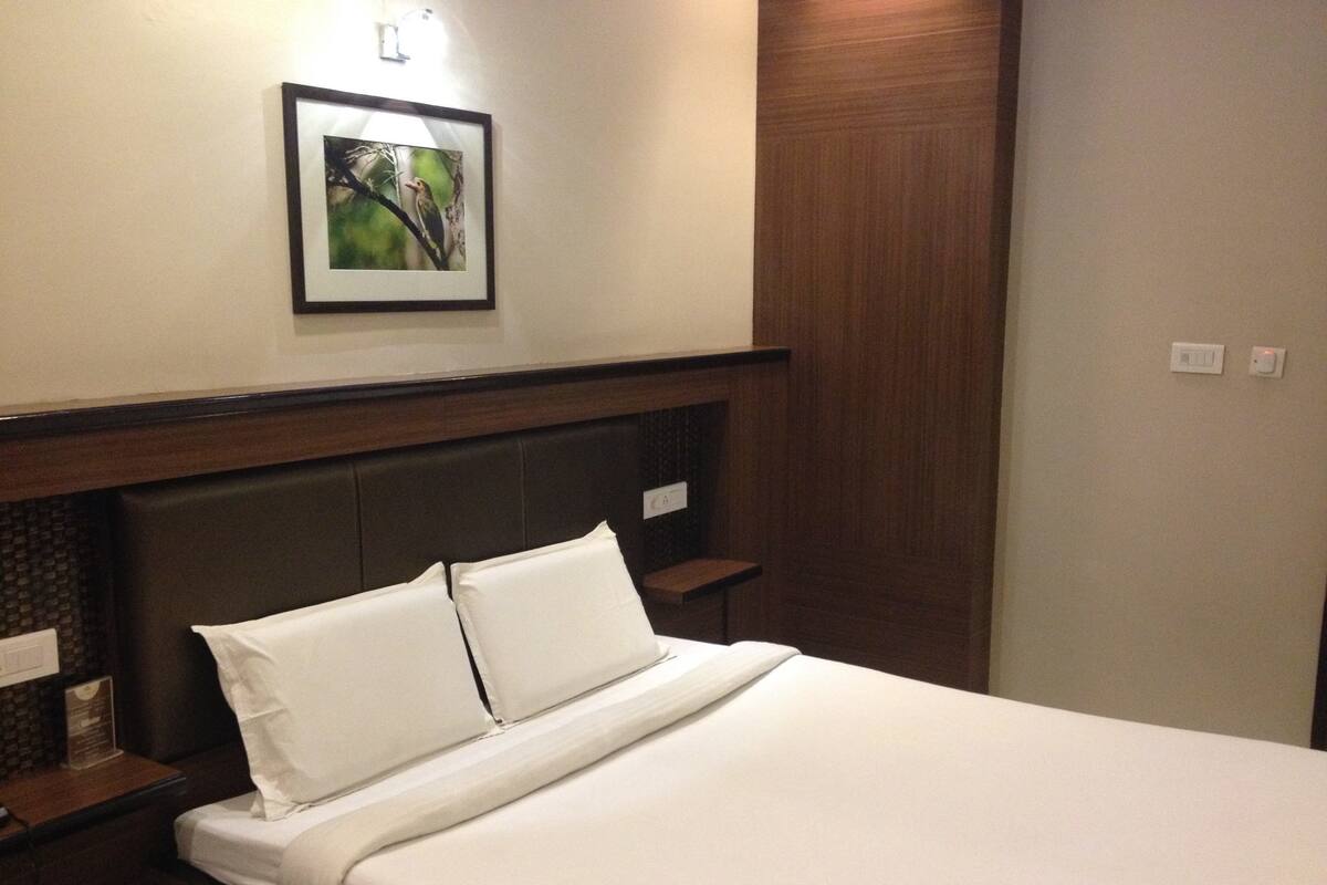 A hotel room with a bed, a headboard, a framed picture on the wall, and a wooden panel.
