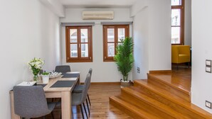 A modern dining area with a wooden table, grey chairs, and a potted plant. - Agora Suites  - Stay in the HEART of CHANIA (Χανιά)