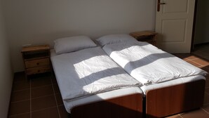 A single bed with a wooden frame and white bedding in a room with tiled flooring and a white door. - Apartmány Horná Seč (Horná Sec)